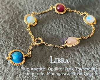 May include: Gold bracelet with five gemstones: blue apatite, opalite, pink tourmaline, moonstone, and Madagascar rose quartz. The bracelet has a clasp and is labeled "LIBRA".