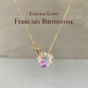 May include: A gold chain necklace with a pendant made of clear and amethyst beads. The pendant is in the shape of a circle and says "Endless Love - February Birthstone".