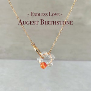 May include: Gold chain necklace with a charm made of clear and orange beads. The charm is in the shape of a circle with the text "Endless Love - August Birthstone" on the image.