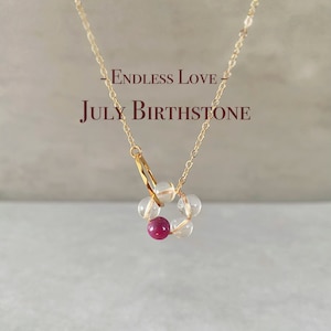Peut inclure: Collier en chaîne dorée avec un pendentif composé de perles transparentes et rouges. Le pendentif est en forme de cercle et porte l'inscription "Endless Love - July Birthstone".