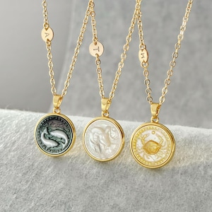 May include: Three gold-tone necklaces featuring circular pendants with zodiac symbols. The left pendant shows Pisces, the center shows Aries, and the right shows Cancer. Each chain includes a small round charm engraved with a single letter.