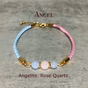 Könnte beinhalten: Ein hellblaues und rosafarbenes geflochtenes Lederarmband mit goldenen Akzenten und drei Edelsteinperlen. Die Perlen sind hellblau, rosa und hellblau. Der Text "ANGELLITE. ROSE QUARTZ." befindet sich unterhalb des Armbands.
