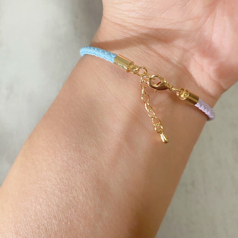 May include: A light blue and lavender braided leather bracelet with a gold clasp and extender chain.
