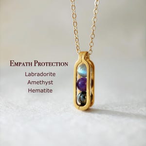 May include: Gold necklace with a pendant containing three stones: labradorite, amethyst, and hematite. The pendant is labelled "Empath Protection".