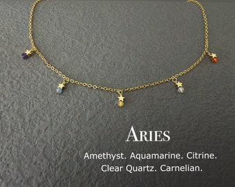 May include: Gold chain necklace with five gemstone charms, including amethyst, aquamarine, citrine, clear quartz, and carnelian. The charms are attached to small gold stars. The necklace is labeled "Aries".