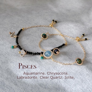Può includere: Un braccialetto con perline nere, una catena dorata e ciondoli con diverse pietre preziose, tra cui acquamarina, crisocolla, labradorite, quarzo trasparente e iolite. Il braccialetto ha una chiusura scorrevole e il testo "Pisces" è scritto sotto il braccialetto.
