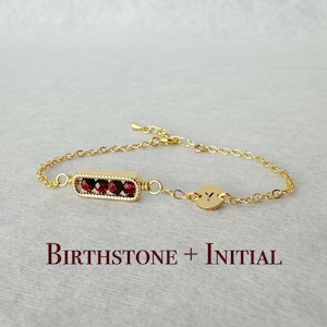 May include: Gold chain bracelet with a red gemstone bar and a gold charm with the letter Y. Birthstone + Initial.