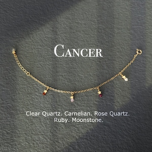 May include: Gold chain bracelet with star charms and gemstone beads. The stones are clear quartz, carnelian, rose quartz, ruby, and moonstone. The bracelet is labeled "Cancer".