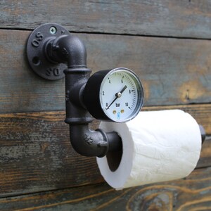 Le dérouleur de papier en fonte est décoré d'un manomètre de pression. Le dérouleur de papier est fixé sur un mur en bois à l'aide d'une bride murale ronde.