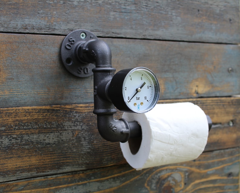 Le dérouleur de papier en fonte est décoré d'un manomètre de pression. Le dérouleur de papier est fixé sur un mur en bois à l'aide d'une bride murale ronde.