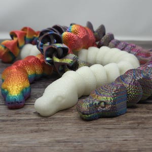Peut inclure: Une collection de jouets en forme de serpent colorés, texturés et à motifs. Les jouets sont faits d'un matériau flexible et sont disposés en pile.