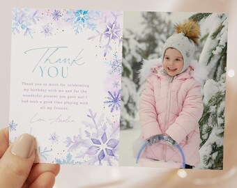 May include: A folded thank you card held by a hand. The card features a photo of a child in a pink coat and a winter scene. The left side has a watercolor design with snowflakes and the words "Thank You".