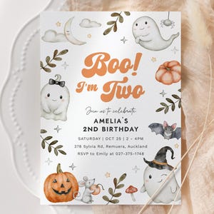 May include: A Halloween-themed invitation card with the text "Boo! I'm Two" in orange. The card features illustrations of ghosts, pumpkins, bats, and a spider. The text also includes the date, time, and location for Amelia's 2nd birthday.
