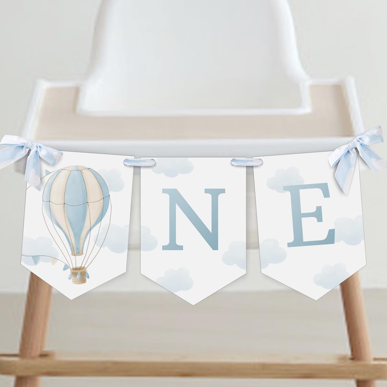 May include: A blue and white hot air balloon banner with the word "ONE" in blue letters. The banner is decorated with white clouds and is perfect for a first birthday party.