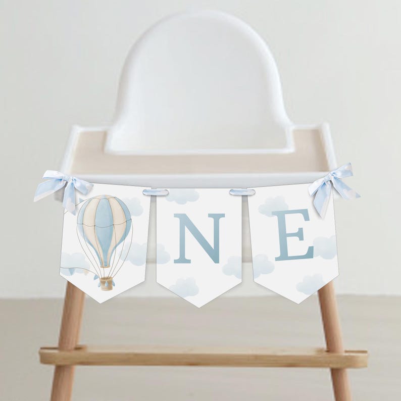 May include: A blue and white hot air balloon high chair banner with the word "ONE" in blue letters. The banner is decorated with white clouds and blue ribbons.