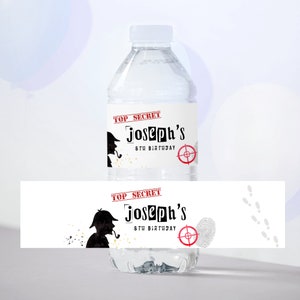 Könnte beinhalten: Wasserflaschenetikett mit Detektiv-Motiv. Das Etikett ist weiß mit schwarzem und rotem Text, der "Top Secret Joseph's 8th Birthday" lautet. Es zeigt die Silhouette eines Detektivs mit einer Lupe und einer Pfeife.