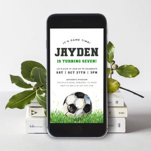 May include: A digital invitation for a soccer-themed birthday party. The invitation is displayed on a smartphone screen and features a green and white soccer ball on a green grass background. The text on the invitation reads "It's Game Time! Jayden is turning seven! Let's kick it! Join us to celebrate Sat | Oct 27th | 3pm Jayden's Stadium 378 Sylvia Road, Remuera, TX 34523 RSVP to Emily at 027-375-1748"
