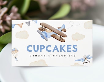May include: A blue and brown airplane with white clouds and a banner in the background. The text "CUPCAKES banana & chocolate" is written below the airplane.