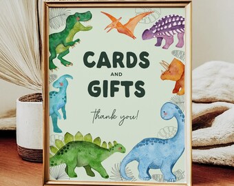 May include: A green and gold frame with a light green background. The frame has a sign that says "Cards and Gifts Thank You!" with a variety of colorful dinosaurs surrounding the text.