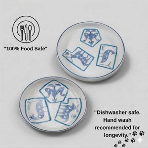May include: Two white ceramic plates with blue patterned designs and blue rims. Each plate features three unique blue illustrations. Text on the image reads "100% Food Safe" and "Dishwasher safe. Hand wash recommended for longevity."
