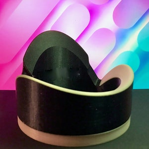May include: A black and white 3D printed object with a curved shape. The object is sitting on a dark surface in front of a colorful background.