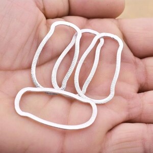 May include: Three silver metal rings, each with a slightly different oval shape, are stacked on top of each other.