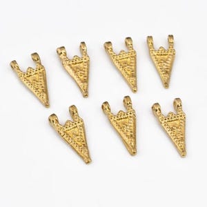Puede incluir: Siete colgantes triangulares dorados con superficie texturizada y parte superior de tres bucles. Los colgantes están dispuestos sobre un fondo blanco. Estos pequeños colgantes decorativos son adecuados para la fabricación de joyas.