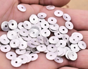May include: A pile of silver-colored metal round beads with a hole in the center. The beads have a textured surface.