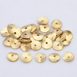 May include: A pile of gold-colored metal beads with a hole in the center. The beads are round and have a slightly textured surface.