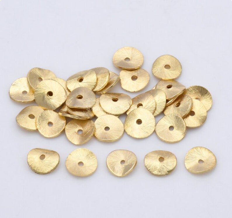 May include: A pile of gold-colored metal beads with a hole in the center. The beads are round and have a slightly textured surface.