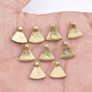Puede incluir: Diez colgantes de metal de color dorado con forma de pequeños hachas. Los colgantes tienen una superficie texturizada y un bucle en la parte superior para colgar.