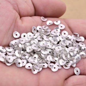 Peut inclure: Un tas de perles en métal de couleur argent, chaque perle est un disque plat avec un trou au centre.