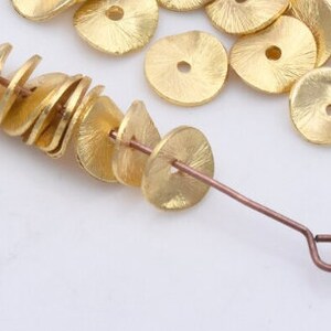 May include: A close-up of a gold wire with a series of gold metal discs strung on it. The discs are flat and have a textured surface. There are several more discs scattered around the wire.