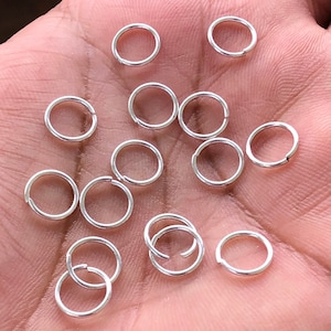 以下が含まれることがあります： 銀製のジャンプリングの山をクローズアップした写真。リングは小さく丸く、ジュエリー作りに最適です。