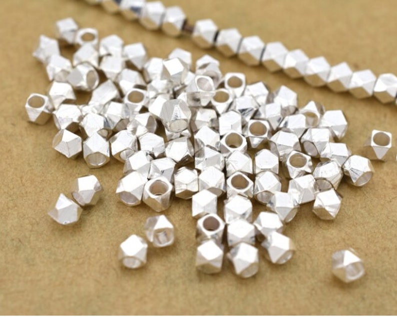 May include: A large pile of silver metal beads with a hole in the center of each bead. The beads are shaped like a multifaceted diamond.