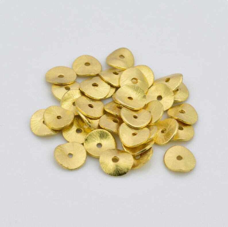 May include: A pile of gold-colored metal beads, each bead is a flat disc with a small hole in the center. The beads have a slightly textured surface.