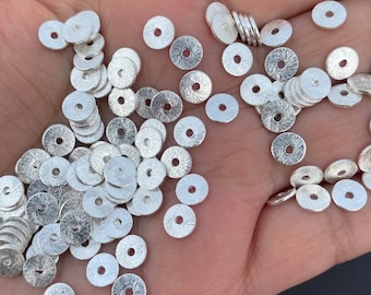 May include: A large pile of silver-toned metal spacer beads. The beads are round with a hole in the center. The beads have a textured surface.