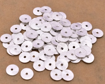 May include: A pile of silver-colored metal spacer beads. The beads are round with a hole in the center. They are about 1/2 inch in diameter.