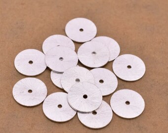 May include: A pile of silver metal discs with a small hole in the center of each disc.