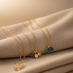 Puede incluir: Collares dorados con colgantes de piedras preciosas de colores sobre una tela beige. Los colgantes presentan piedras rojas, blancas, amarillas, verdes y azules. Los collares tienen delicadas cadenas de oro.