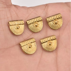 May include: Five gold-toned metal pendant charms with a rounded, half-circle shape. Each charm has a raised, textured design with concentric circles and a small, round bead in the center.