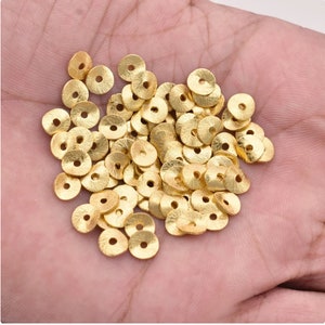 Peut inclure: Un grand tas de perles rondes en métal couleur or avec un petit trou au centre. Les perles ont une surface texturée.