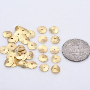 May include: A pile of 20 gold-colored metal beads with a hole in the center. The beads are about the size of a US quarter.