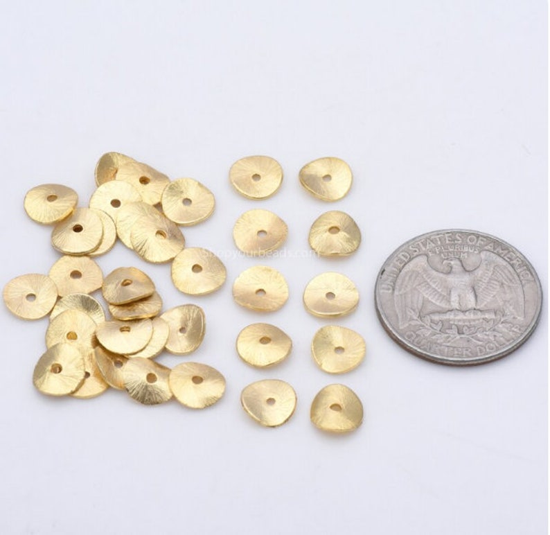 May include: A pile of 20 gold-colored metal beads with a hole in the center. The beads are about the size of a US quarter.