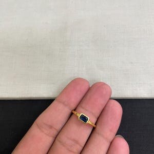 Peut inclure: Une bague en or ornée d'une pierre précieuse bleu profond de taille rectangulaire, fixée dans un serti clos. L'anneau est fin et poli, présentant un design épuré qui met en valeur le contraste entre la pierre bleue vive et le métal en or jaune.