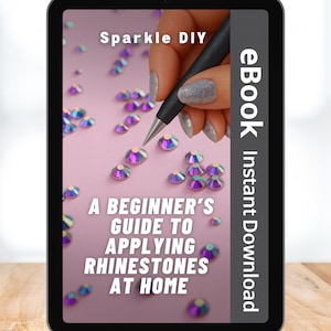 May include: A digital tablet displays an ebook titled "A Beginner's Guide to Applying Rhinestones at Home." The cover features the text "Sparkle DIY" and a hand holding a rhinestone applicator over scattered iridescent rhinestones on a pink background.