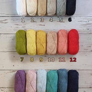 18 different colors of yarn to choose from for toddler name sweater are lined up on the floor.  White, ecru, beige, tan, grey, black, olive, yellow, mustard, pastel peach, coral, red, purple, lavender, light blue, turquoise, denim blue, navy blue.