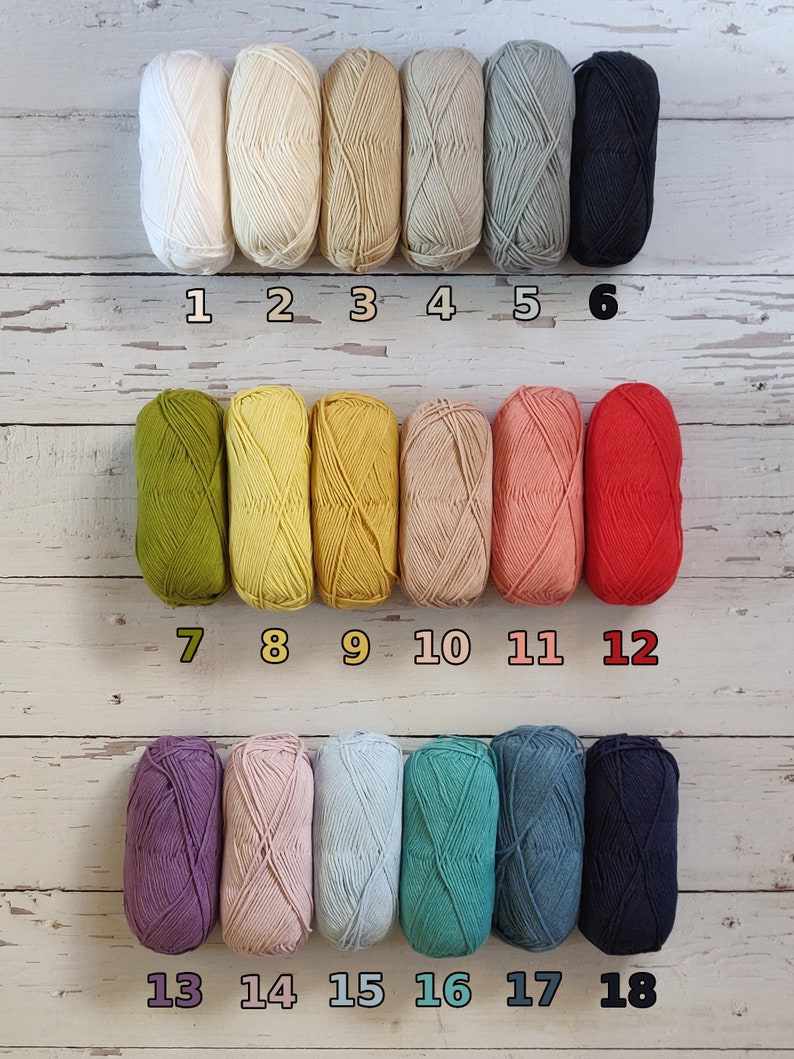 18 different colors of yarn to choose from for toddler name sweater are lined up on the floor.  White, ecru, beige, tan, grey, black, olive, yellow, mustard, pastel peach, coral, red, purple, lavender, light blue, turquoise, denim blue, navy blue.