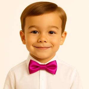 May include: A young child wearing a white button-down shirt and a bright magenta bow tie. The bow tie is centered and adds a pop of color against the white shirt. The child is smiling.