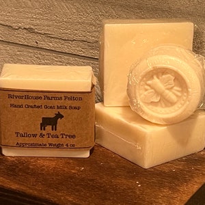 May include: Three bars of hand-crafted goat milk soap, one with a bee design and the others wrapped in brown paper with the text "RiverHouse Farms Felton Hand Crafted Goat Milk Soap Tallow & Tea Tree Approximate Weight 4 oz"